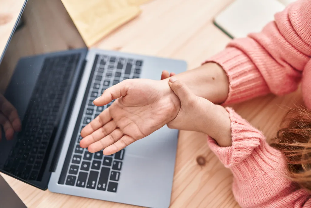 Office worker holding their wrist near a laptop, showing hand and wrist discomfort commonly associated with carpal tunnel syndrome