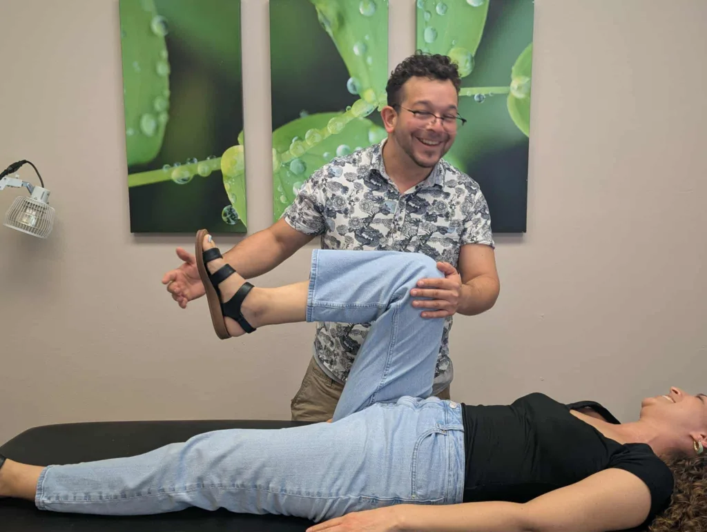 Acupuncturist performing hip flexion mobility assessment on a patient during treatment session.